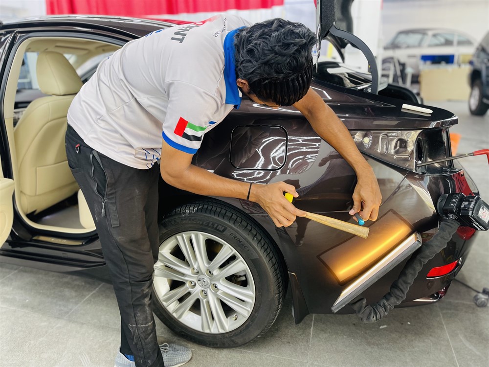 Technician performing paintless dent repair on accident-damaged car panel in Dubai